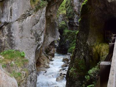 A view of a narrow, rocky gorge with a rushing stream, featuring a wooden walkway and tunnel entrance on the right side.