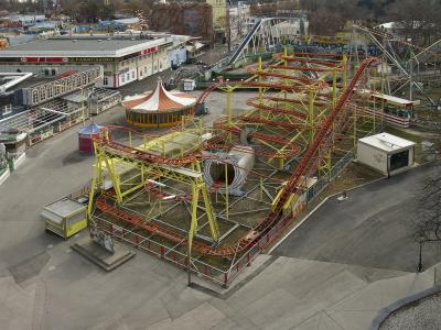 An aerial view of a yellow and red roller coaster track with a large snake-themed tunnel, situated within a larger amusement park complex that includes a building labeled "PARKCASINO" and other rides.