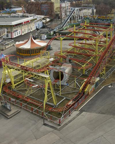 An aerial view of a yellow and red roller coaster track with a large snake-themed tunnel, situated within a larger amusement park complex that includes a building labeled "PARKCASINO" and other rides.