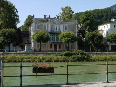 A large, classical-style yellow building with white trim stands on the bank of a green river, featuring prominent signage on its facade that reads "LEHAR VILLA".