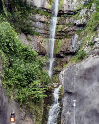 A waterfall cascading down a rocky cliff face, with a road, traffic light, stop sign, and lamp post visible in the foreground.