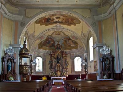 The image shows a large, ornate wooden altarpiece with multiple gilded statues of saints, situated inside a church with painted vaulted ceilings and frescoes on the walls.