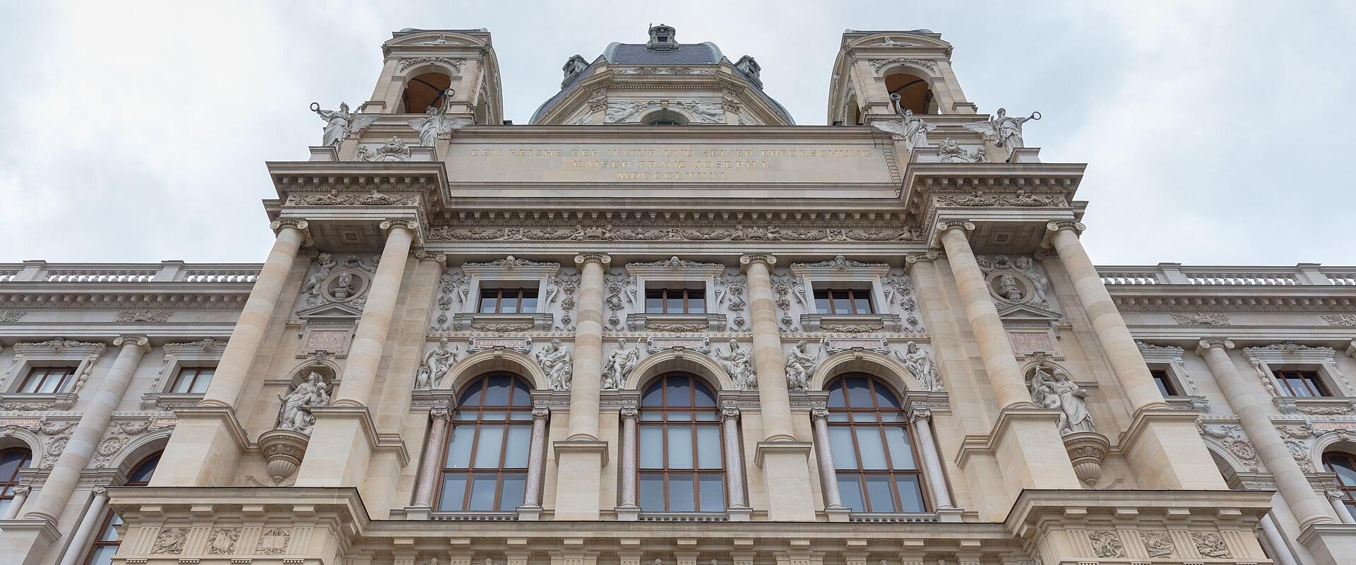 The image shows the ornate neoclassical facade of a grand museum building with large arched windows, sculptural reliefs, and a central dome, identified by its architecture as the Naturhistorisches Museum in Vienna, Austria.