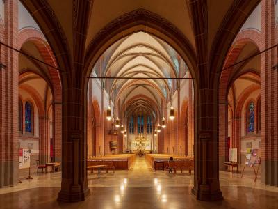 The interior of a large brick church with pointed arches, ribbed vaults, stained glass windows, and rows of wooden pews leading to an altar.