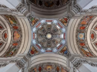 The image shows an ornate, high-ceilinged interior with a central octagonal dome, elaborate white stucco work, and numerous religious frescoes on the vaults and pendentives, characteristic of Baroque church architecture.