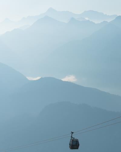 A cable car (gondola) suspended on cables against a backdrop of layered, hazy blue mountain ranges.