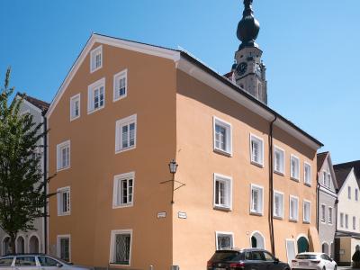 A large, peach-colored building with white-framed windows stands on a cobblestone street corner, with a church tower featuring a dark onion dome visible behind it.