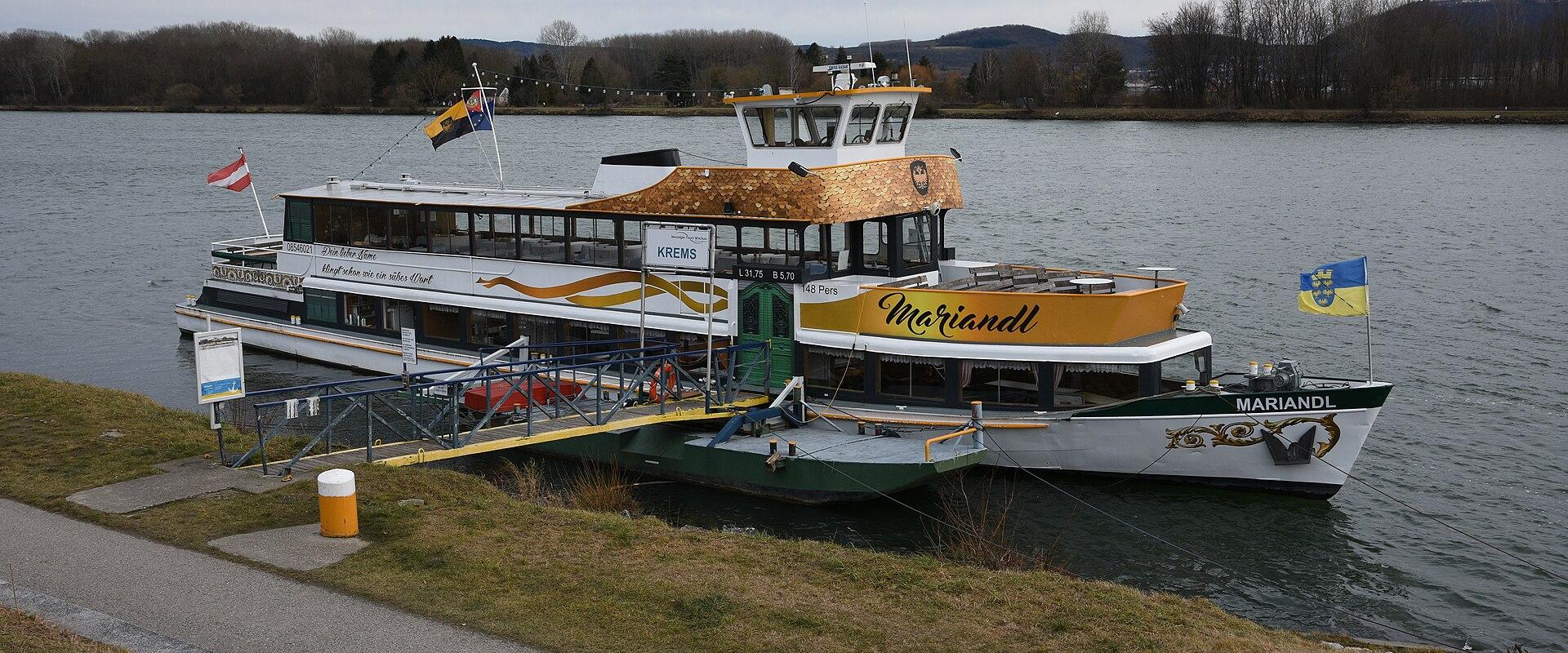 A passenger boat named "Mariandl" is docked at a riverside pier in Krems, Austria, with visible signage including "KREMS" and the boat’s name on its hull and superstructure.