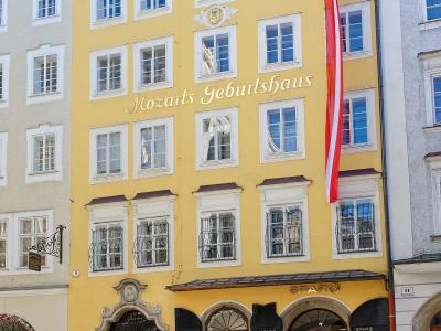 A yellow multi-story building on a paved street corner with a large red and white Austrian flag, featuring the text "Mozarts Geburtshaus" in gold lettering on the facade and a SPAR supermarket on the ground floor.