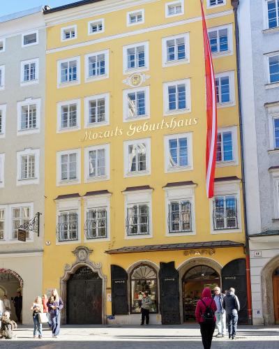 A yellow multi-story building on a paved street corner with a large red and white Austrian flag, featuring the text "Mozarts Geburtshaus" in gold lettering on the facade and a SPAR supermarket on the ground floor.